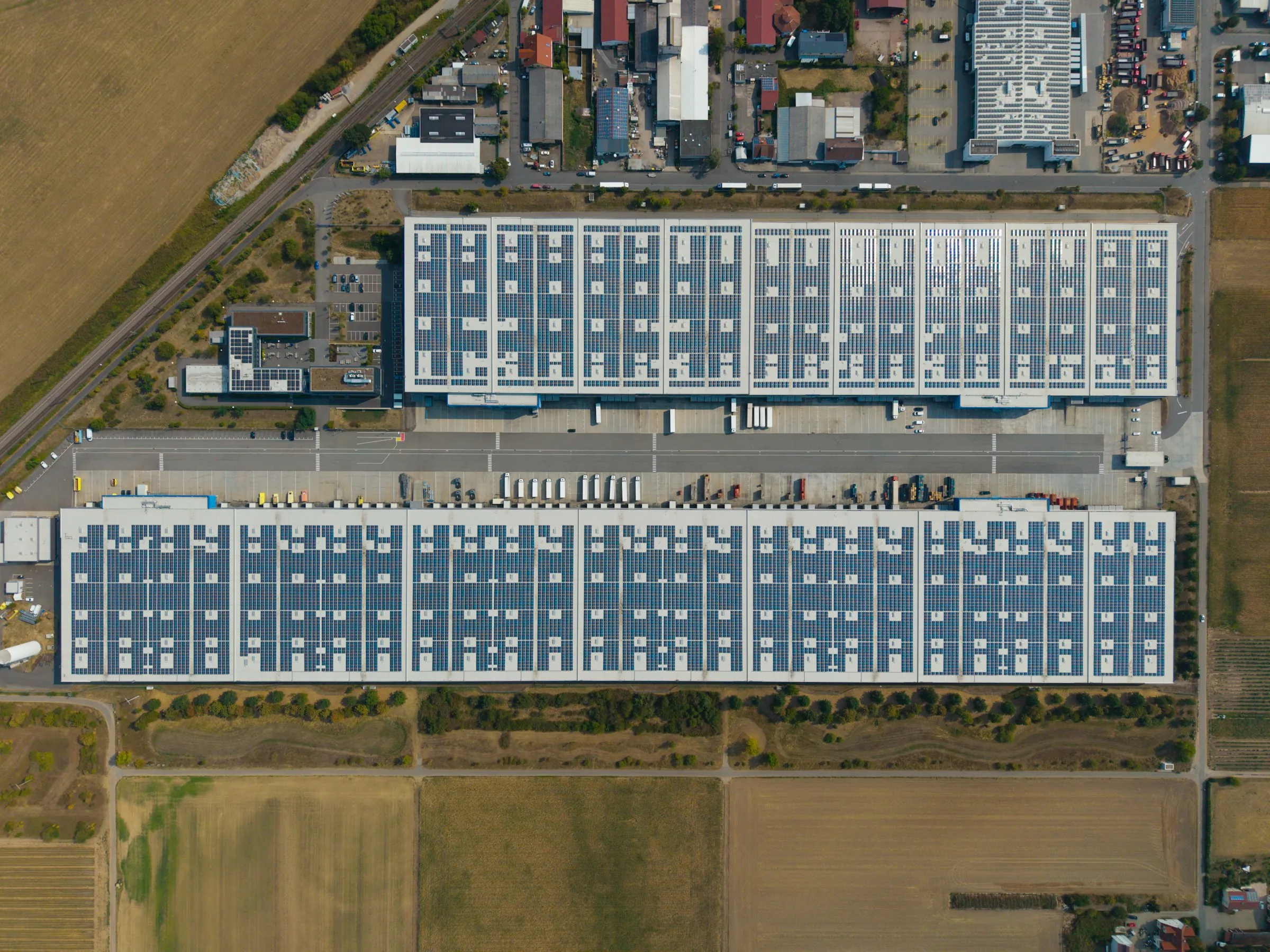 Luchtfoto recht van boven van twee grote distributiecentra met zonnepanelen op de daken en vrachtwagens aan de laaddocks